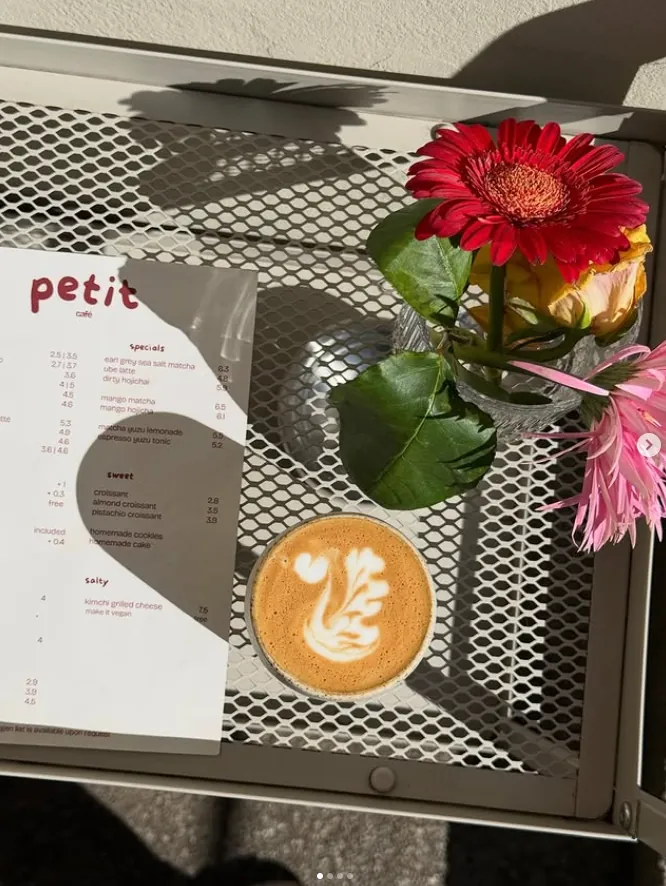 Sonniger Tisch im Café Petit mit Latte, Blumen und der Karte